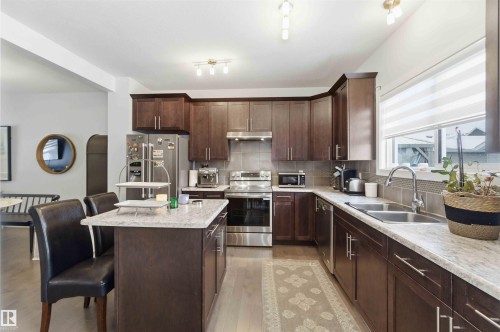 Kitchen featuring stainless steel appliances, a kitchen island, dark wood finish cabinets, a breakfast bar area, and light stone countertops - 2331 71 Street, Edmonton, AB - Indoor Photo Showing Kitchen With Stainless Steel Kitchen With Double Sink