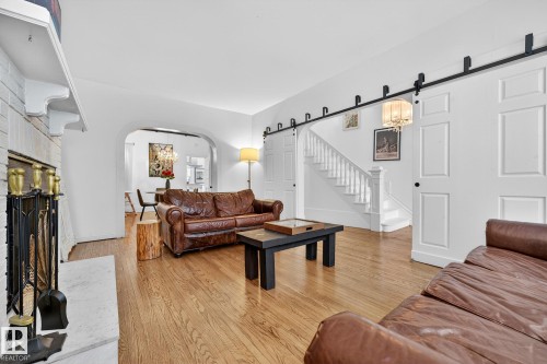 Living room featuring a barn door, suspended lighting, light wood-style floors, arched walkways, and a large fireplace - 10523 127 Street, Edmonton, AB - Indoor Photo Showing Living Room