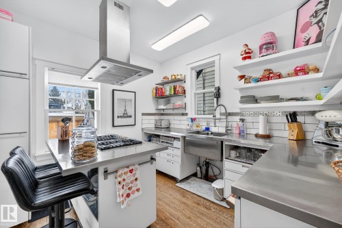 Kitchen featuring stainless steel counters, white cabinets, a kitchen bar, island range hood, and light wood finished floors - 10523 127 Street, Edmonton, AB - Indoor Photo Showing Office