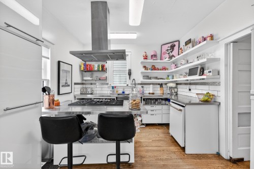 Kitchen featuring stainless steel countertops, white cabinets, island exhaust hood, and light wood-style flooring - 10523 127 Street, Edmonton, AB - Indoor