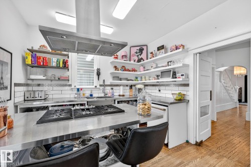 Kitchen with island exhaust hood, arched walkways, light wood finished floors, stainless steel counters, and backsplash - 10523 127 Street, Edmonton, AB - Indoor Photo Showing Other Room
