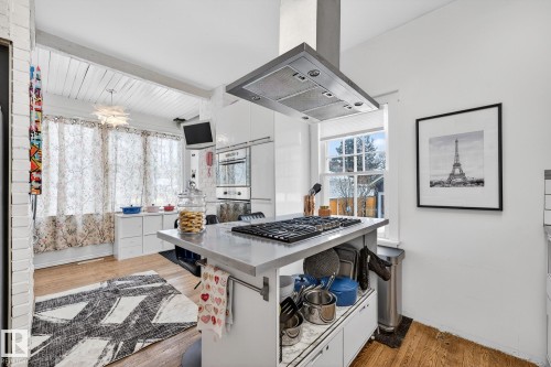 Kitchen featuring island exhaust hood, white cabinets, light wood-type flooring, stainless steel gas cooktop, and plenty of natural light - 10523 127 Street, Edmonton, AB - Indoor Photo Showing Other Room