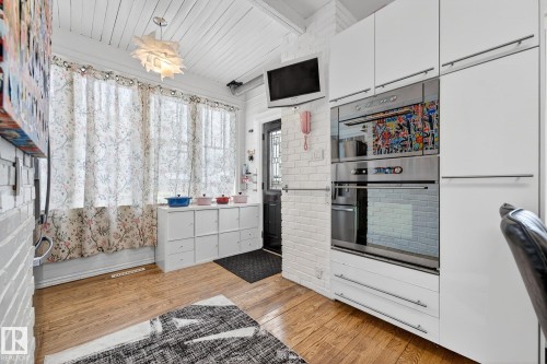 Kitchen featuring stainless steel double oven, white cabinets, light wood-style floors, light countertops, and a wood ceiling with exposed beams - 10523 127 Street, Edmonton, AB - Indoor
