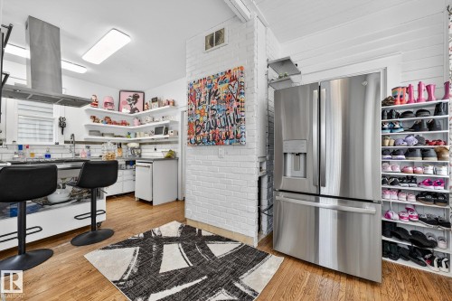 Kitchen with stainless steel fridge, brick wall, island range hood, light wood-style floors, and white dishwasher - 10523 127 Street, Edmonton, AB - Indoor