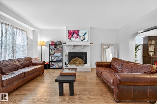 Living area with a brick fireplace, hardwood / wood-style floors, arched walkways, and plenty of natural light - 10523 127 Street, Edmonton, AB - Indoor Photo Showing Living Room With Fireplace