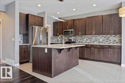 Kitchen with stainless steel appliances, a kitchen bar, light wood-type flooring, light stone countertops, and an island with sink - 7515 178 Avenue, Edmonton, AB - Indoor Photo Showing Kitchen With Upgraded Kitchen