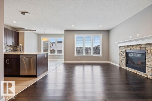 Kitchen with dark wood finish cabinets, open floor plan, dishwasher, light wood-style flooring, and a textured ceiling - 7515 178 Avenue, Edmonton, AB - Indoor Photo Showing Living Room With Fireplace