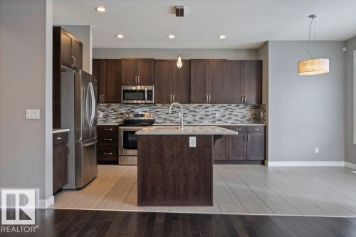 Kitchen with stainless steel appliances, light stone countertops, light wood finished floors, dark wood finish cabinetry, and a textured ceiling - 7515 178 Avenue, Edmonton, AB - Indoor Photo Showing Kitchen With Upgraded Kitchen
