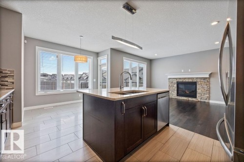 Kitchen with dark wood finish cabinets, a textured ceiling, a fireplace, stainless steel appliances, and pendant lighting - 7515 178 Avenue, Edmonton, AB - Indoor Photo Showing Kitchen With Double Sink