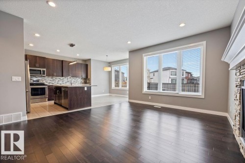 Unfurnished living room with a stone fireplace, light wood finished floors, recessed lighting, and a textured ceiling - 7515 178 Avenue, Edmonton, AB - Indoor Photo Showing Kitchen With Upgraded Kitchen