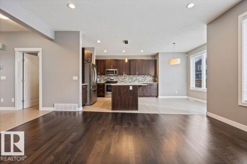 Kitchen with dark wood finish cabinetry, light wood-type flooring, an island with sink, stainless steel appliances, and decorative light fixtures - 7515 178 Avenue, Edmonton, AB - Indoor Photo Showing Kitchen With Upgraded Kitchen