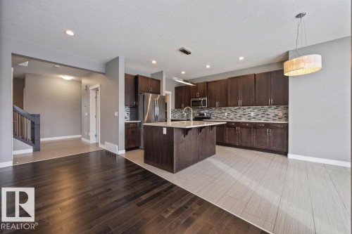 Kitchen with a kitchen breakfast bar, a center island with sink, light wood finished floors, decorative light fixtures, and stainless steel microwave - 7515 178 Avenue, Edmonton, AB - Indoor Photo Showing Kitchen With Upgraded Kitchen