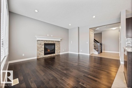 Unfurnished living room with a stone fireplace, dark wood finished floors, and recessed lighting - 7515 178 Avenue, Edmonton, AB - Indoor Photo Showing Living Room With Fireplace