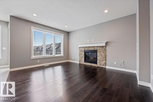 Unfurnished living room featuring a textured ceiling, a stone fireplace, dark wood finished floors, and recessed lighting - 7515 178 Avenue, Edmonton, AB - Indoor Photo Showing Living Room With Fireplace