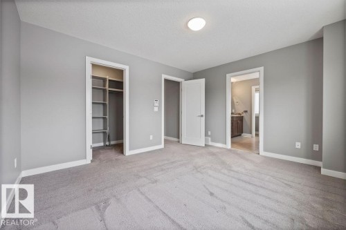 Unfurnished bedroom featuring a walk in closet, a textured ceiling, light colored carpet, and connected bathroom - 7515 178 Avenue, Edmonton, AB - Indoor Photo Showing Other Room