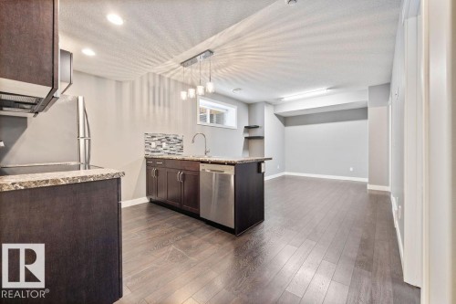Kitchen featuring dark wood finish cabinetry, a peninsula, light stone counters, a textured ceiling, and dishwasher - 7515 178 Avenue, Edmonton, AB - Indoor