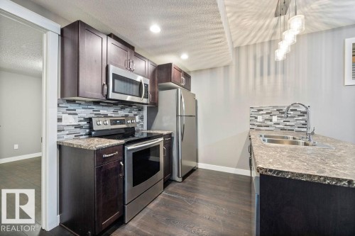Kitchen featuring stainless steel appliances, tasteful backsplash, dark wood-style flooring, dark wood finish cabinets, and a textured ceiling - 7515 178 Avenue, Edmonton, AB - Indoor Photo Showing Kitchen With Double Sink