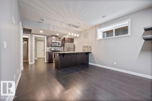 Kitchen with a peninsula, a kitchen bar, tasteful backsplash, stainless steel appliances, and dark wood finish cabinets - 7515 178 Avenue, Edmonton, AB - Indoor Photo Showing Other Room