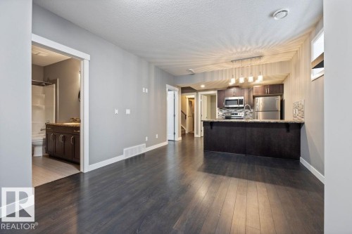 Kitchen with a peninsula, light stone counters, stainless steel appliances, dark wood-type flooring, and a kitchen breakfast bar - 7515 178 Avenue, Edmonton, AB - Indoor Photo Showing Kitchen
