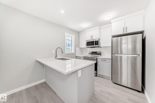 Kitchen featuring stainless steel appliances, a peninsula, white cabinetry, a breakfast bar area, and light wood-style floors - 3323 Roy Brown Way, Edmonton, AB - Indoor Photo Showing Kitchen With Stainless Steel Kitchen