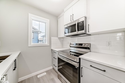Kitchen with stainless steel appliances, white cabinets, backsplash, and light wood-type flooring - 3323 Roy Brown Way, Edmonton, AB - Indoor Photo Showing Kitchen