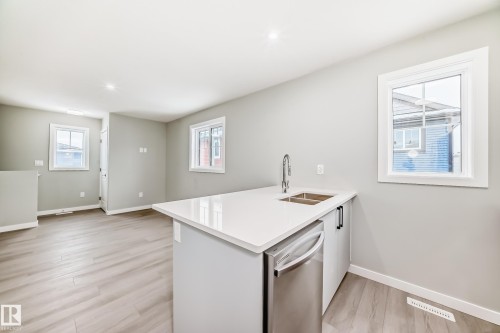 Kitchen with a peninsula, stainless steel dishwasher, light wood-style flooring, light stone counters, and white cabinetry - 3323 Roy Brown Way, Edmonton, AB - Indoor Photo Showing Kitchen With Double Sink