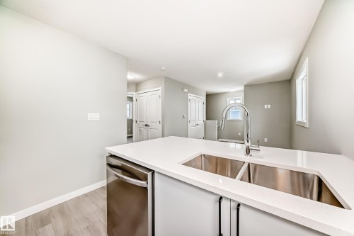 Kitchen featuring stainless steel dishwasher, light wood-type flooring, and light stone counters - 3323 Roy Brown Way, Edmonton, AB - Indoor Photo Showing Kitchen With Double Sink