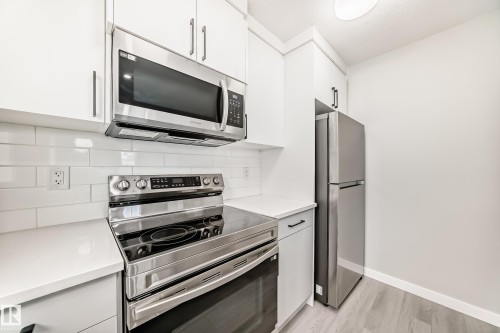 Kitchen featuring stainless steel appliances, white cabinets, light wood-style flooring, and tasteful backsplash - 3323 Roy Brown Way, Edmonton, AB - Indoor Photo Showing Kitchen With Stainless Steel Kitchen