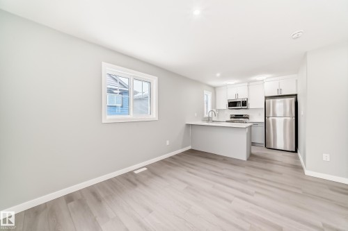 Kitchen featuring a peninsula, stainless steel appliances, white cabinets, and light wood finished floors - 3323 Roy Brown Way, Edmonton, AB - Indoor Photo Showing Kitchen