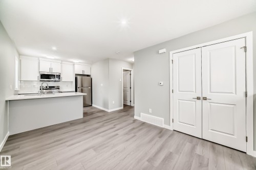 Kitchen featuring white cabinetry, stainless steel appliances, a peninsula, light wood-style flooring, and light stone countertops - 3323 Roy Brown Way, Edmonton, AB - Indoor Photo Showing Kitchen