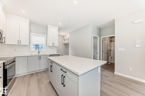 Kitchen featuring electric range, light wood finished floors, a kitchen island, backsplash, and white cabinetry - 3323 Roy Brown Way, Edmonton, AB - Indoor Photo Showing Kitchen