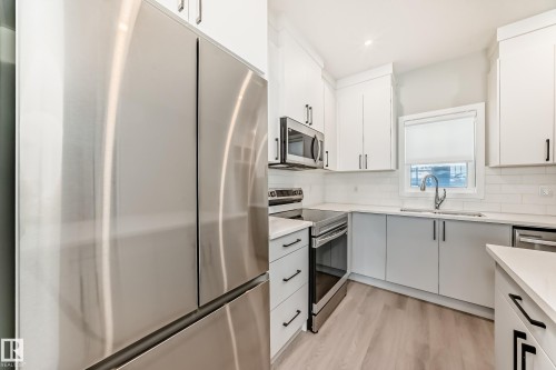 Kitchen with stainless steel appliances, white cabinets, light wood finished floors, backsplash, and recessed lighting - 3323 Roy Brown Way, Edmonton, AB - Indoor Photo Showing Kitchen With Stainless Steel Kitchen With Double Sink With Upgraded Kitchen
