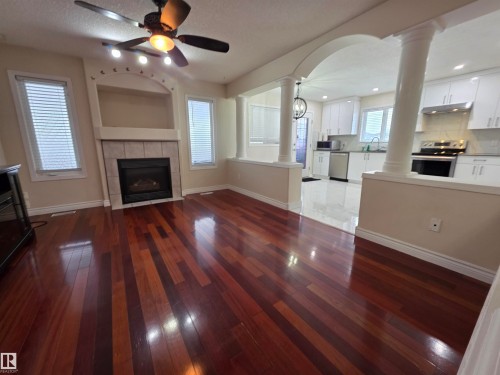 Unfurnished living room featuring decorative columns, arched walkways, dark wood-style floors, and a fireplace - 6731 162 Ave, Edmonton, AB - Indoor With Fireplace