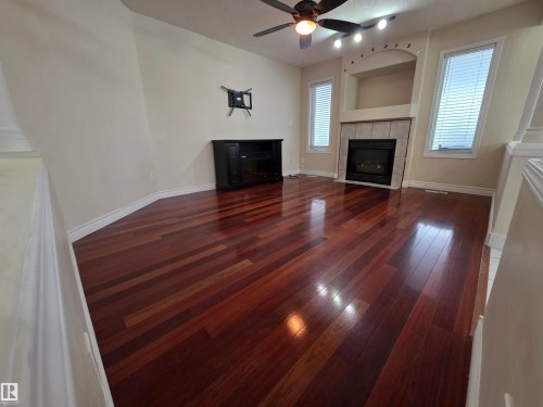 Unfurnished living room featuring a tile fireplace, dark wood-type flooring, and ceiling fan - 6731 162 Ave, Edmonton, AB - Indoor Photo Showing Living Room With Fireplace
