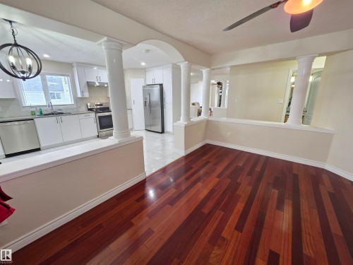 Kitchen featuring stainless steel appliances, white cabinetry, light wood-type flooring, arched walkways, and decorative backsplash - 6731 162 Ave, Edmonton, AB - Indoor Photo Showing Kitchen