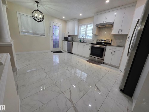 Kitchen with stainless steel appliances, white cabinetry, suspended lighting, dark countertops, and backsplash - 6731 162 Ave, Edmonton, AB - Indoor Photo Showing Kitchen