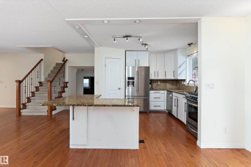 Kitchen with white cabinetry, stainless steel appliances, dark stone countertops, dark wood-style flooring, and a textured ceiling - 115 Walker Road, Edmonton, AB - Indoor Photo Showing Kitchen