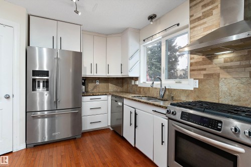 Kitchen with stainless steel appliances, dark stone countertops, dark wood finished floors, white cabinetry, and tasteful backsplash - 115 Walker Road, Edmonton, AB - Indoor Photo Showing Kitchen With Double Sink