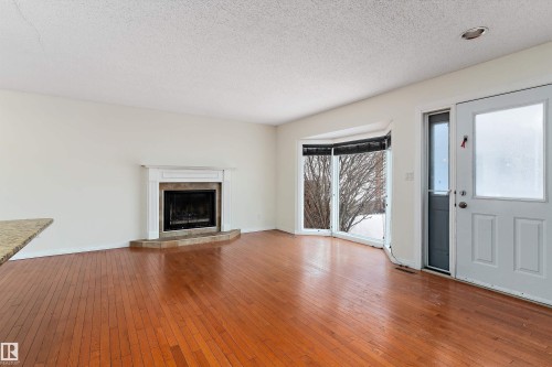Unfurnished living room featuring wood-type flooring, a textured ceiling, and a tiled fireplace - 115 Walker Road, Edmonton, AB - Indoor Photo Showing Living Room With Fireplace