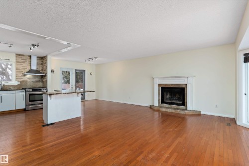 Kitchen with track lighting, open floor plan, dark wood-style floors, decorative backsplash, and a kitchen breakfast bar - 115 Walker Road, Edmonton, AB - Indoor With Fireplace