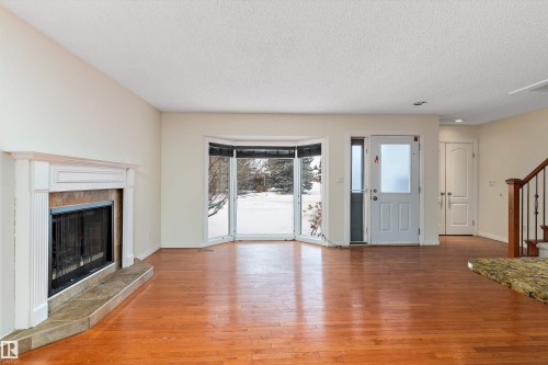 Unfurnished living room featuring light wood-type flooring, a tile fireplace, and a textured ceiling - 115 Walker Road, Edmonton, AB - Indoor Photo Showing Living Room With Fireplace