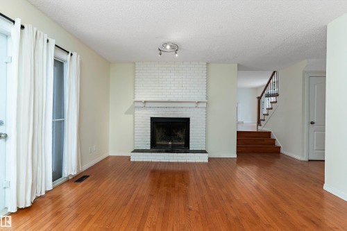 Unfurnished living room with wood-type flooring, a textured ceiling, and a brick fireplace - 115 Walker Road, Edmonton, AB - Indoor Photo Showing Living Room With Fireplace