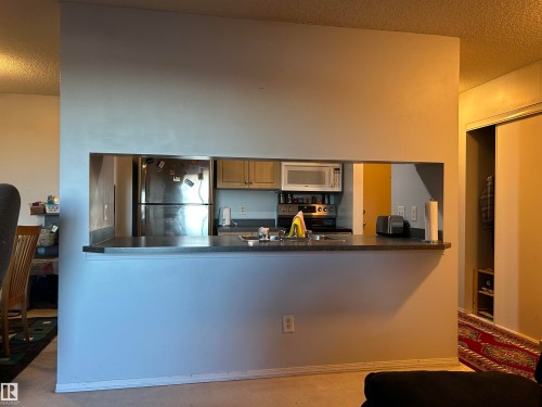 Kitchen featuring stainless steel appliances, a textured ceiling, dark countertops, and a peninsula - 310 2430 Guardian Road, Edmonton, AB - Indoor Photo Showing Kitchen