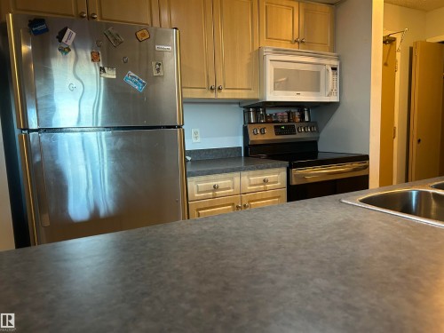 Kitchen with dark countertops and stainless steel appliances - 310 2430 Guardian Road, Edmonton, AB - Indoor Photo Showing Kitchen