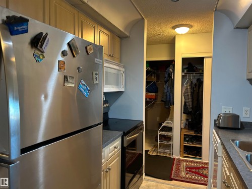 Kitchen featuring freestanding refrigerator, dark countertops, range with electric cooktop, white microwave, and a textured ceiling - 310 2430 Guardian Road, Edmonton, AB - Indoor Photo Showing Kitchen With Double Sink
