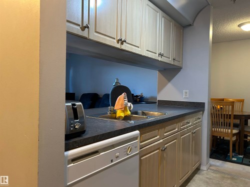 Kitchen featuring dark countertops, white dishwasher, and a textured ceiling - 310 2430 Guardian Road, Edmonton, AB - Indoor Photo Showing Kitchen