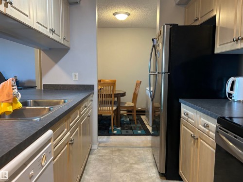 Kitchen with dark countertops, a textured ceiling, white dishwasher, and black electric range oven - 310 2430 Guardian Road, Edmonton, AB - Indoor Photo Showing Kitchen With Double Sink