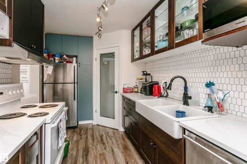 Kitchen with stainless steel appliances, backsplash, glass fronted cabinets, dark wood finished floors, and two tone cabinetry - 407 8149 111 St S, Edmonton, AB - Indoor Photo Showing Kitchen With Double Sink