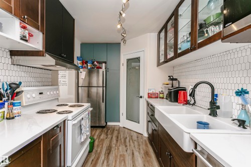 Kitchen with stainless steel appliances, decorative backsplash, glass insert cabinets, light wood finished floors, and two tone cabinetry - 407 8149 111 St S, Edmonton, AB - Indoor Photo Showing Kitchen