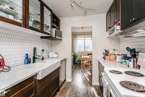 Kitchen featuring dark wood finish cabinetry, electric range, and backsplash - 407 8149 111 St S, Edmonton, AB - Indoor Photo Showing Kitchen With Double Sink
